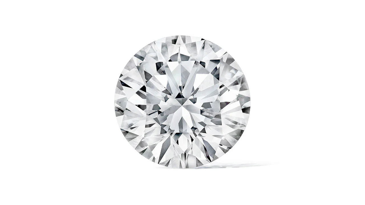Un diamante rotondo taglio brillante con sfaccettature multiple che riflettono la luce, che ricordano i gioielli presenti nell'asta record di Maria Antonietta, incastonato su uno sfondo bianco semplice.