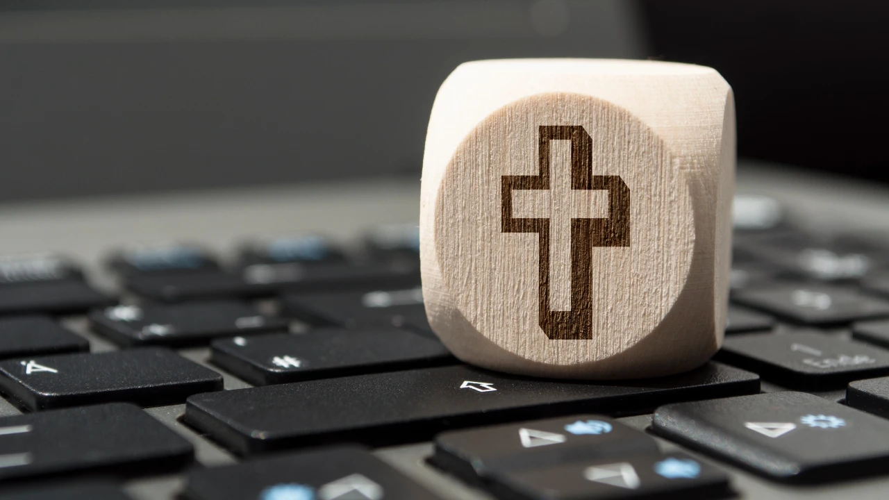 Un blocco di legno con il simbolo di una croce intagliata è appoggiato sui tasti della tastiera di un computer portatile, a rappresentare il futuro dell’eredità digitale.
