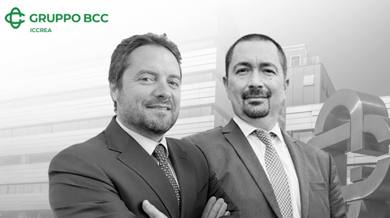 Due uomini in giacca e cravatta sono affiancati, sorridenti, davanti a un edificio moderno. Il logo del Gruppo BCC Iccrea è in alto a sinistra. L'immagine è in bianco e nero.