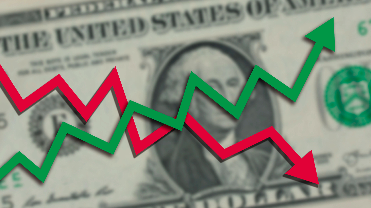 Una banconota da un dollaro USA sfocata sullo sfondo con frecce a zig-zag rosse e verdi sovrapposte che rappresentano le fluttuazioni dell'andamento finanziario o del mercato azionario.