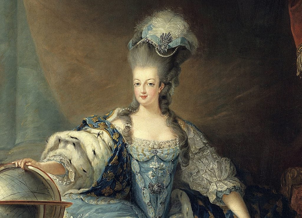 Una donna in un elaborato abito blu e bianco del XVIII secolo con pizzi e dettagli ingioiellati siede accanto a un mappamondo. Indossa un cappello alto e piumato e un mantello foderato di pelliccia, guardando direttamente lo spettatore su uno sfondo scuro.