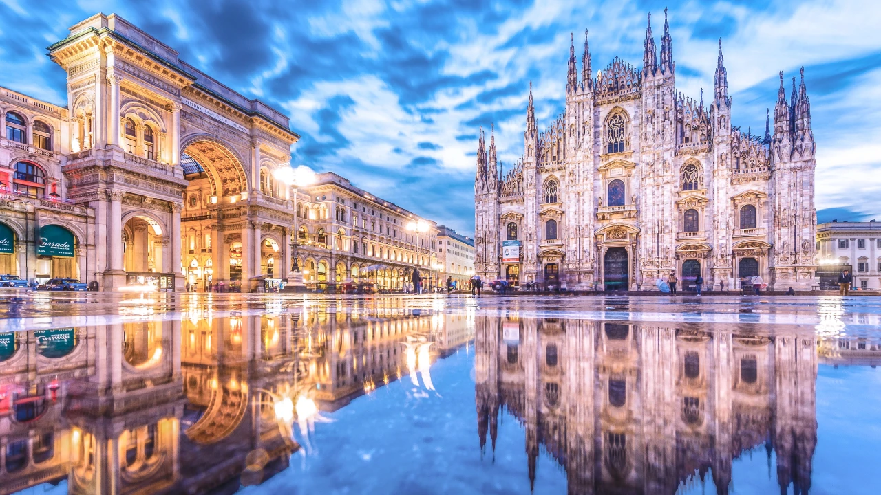 Una veduta della Piazza del Duomo di Milano al tramonto, che mostra il Duomo di Milano illuminato e l'arco della Galleria Vittorio Emanuele.
