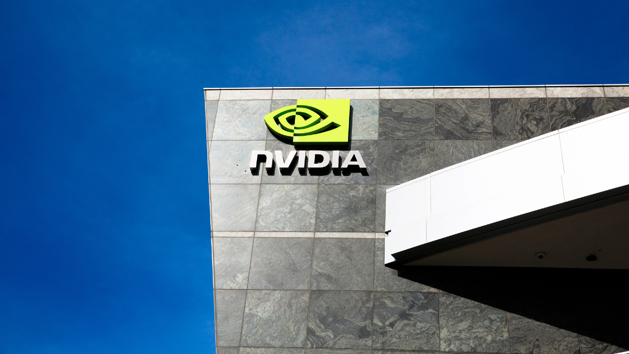 L'esterno di un edificio moderno presenta il logo e il nome di NVIDIA, visualizzati in bianco e verde, su piastrelle grigie con un cielo azzurro sullo sfondo.