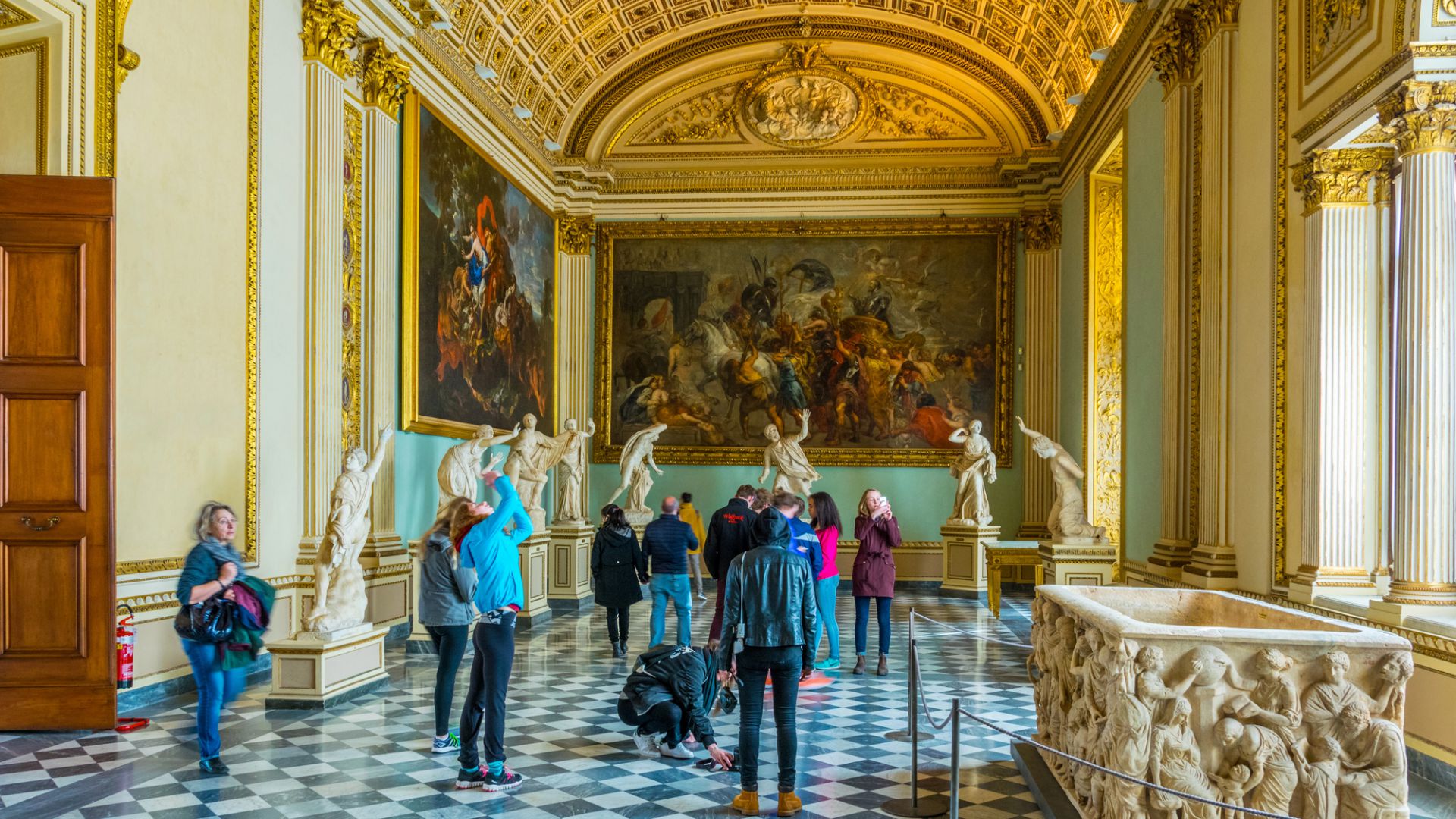 I visitatori si trovano in una galleria museale ornata, un vero e proprio bene di piacere di grande valore, con un pavimento a scacchi, statue di marmo, accenti dorati, alte colonne e soffitti a volta ornati da dipinti classici.