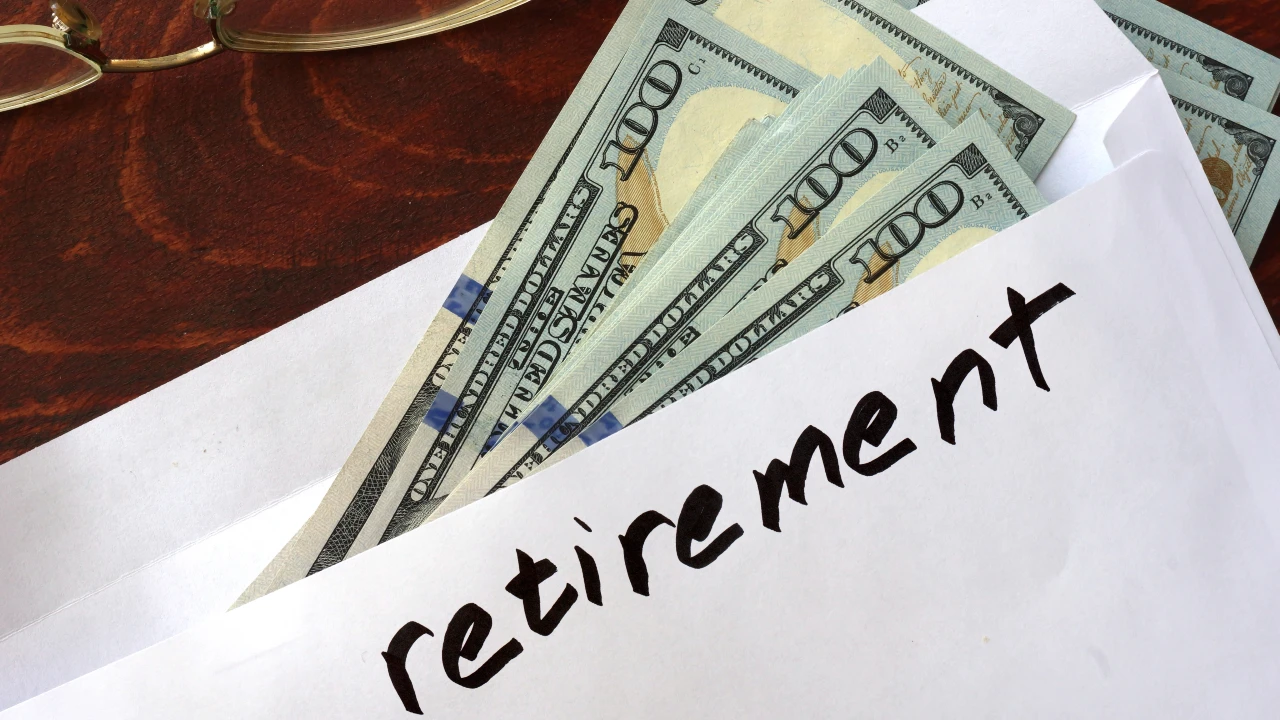 A white envelope labeled "retirement" and holding several hundred-dollar bills, some marked for tax savings, rests on a wooden surface.