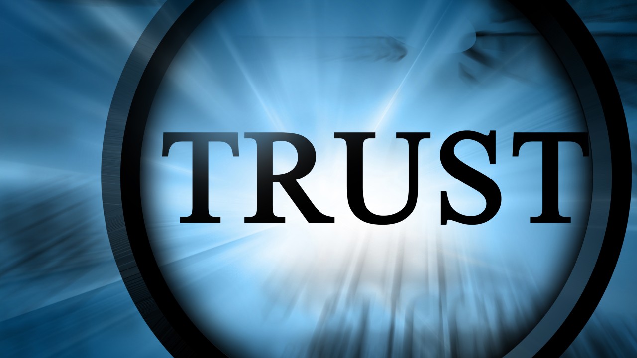 La parola "TRUST", in grassetto e in lettere nere, è centrata su uno sfondo blu con un effetto luminoso e radiante, che dà un senso di importanza e concentrazione.