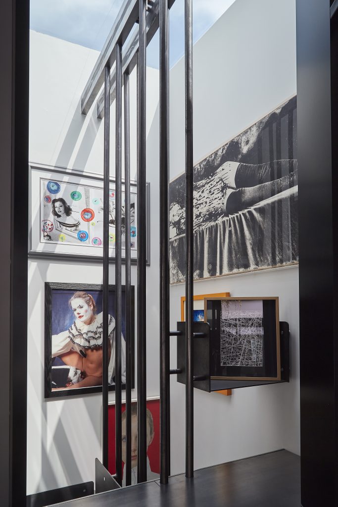 L'interno moderno della Casa Museo Molinario Colombari è caratterizzato da pareti bianche ornate da opere d'arte incorniciate - ritratti e pezzi astratti - disposte intorno a un'alta struttura di ringhiera metallica nera sotto un lucernario.
