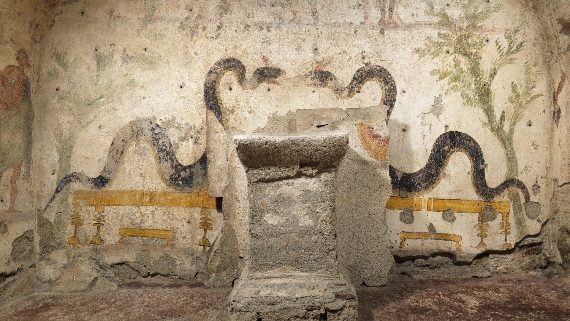 L'antico affresco di Panorama Pozzuoli raffigura due grandi serpenti neri che si fronteggiano, circondando un altare in pietra, con piante e motivi stilizzati su uno sfondo murale materico e sbiadito.