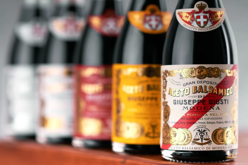 Primo piano di una fila di bottiglie di Aceto Balsamico di Modena Giuseppe Giusti dell'Acetaia Giusti, con una bottiglia a fuoco e le altre sfocate sullo sfondo.