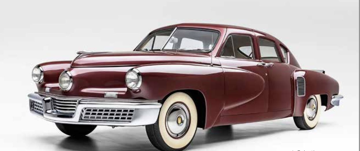 Un'auto vintage di colore marrone con carrozzeria arrotondata, tre fari, ampi pneumatici bianchi e dettagli cromati, visualizzata su uno sfondo bianco.