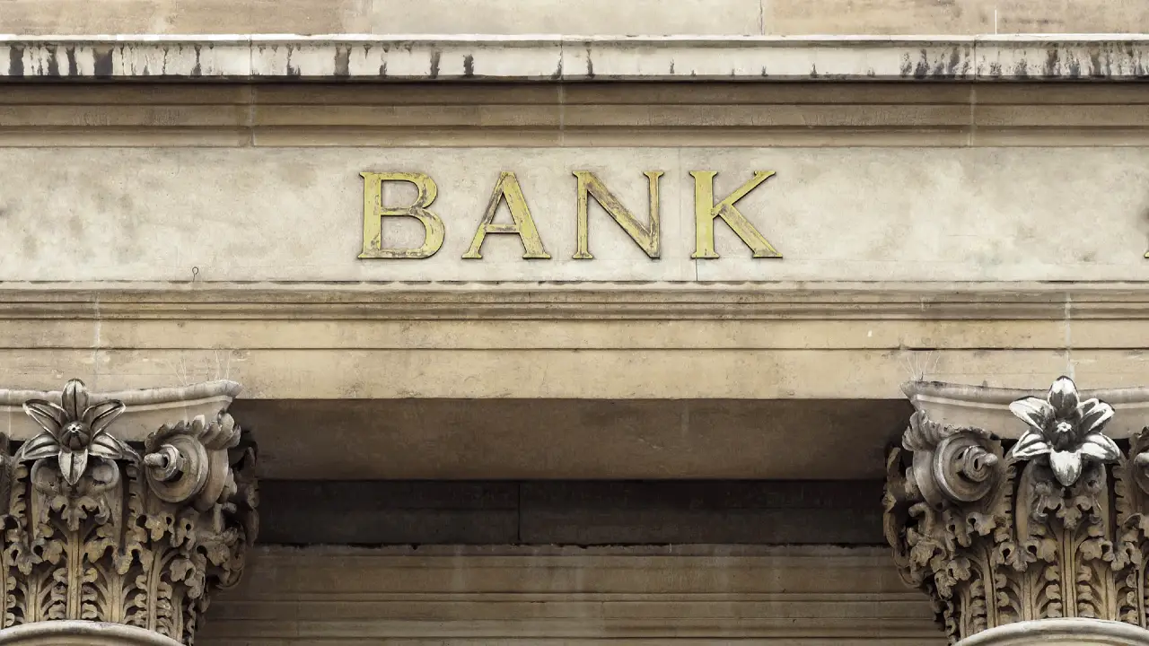 Facciata dell'edificio in pietra con la parola "BANK" incisa in lettere d'oro sopra due colonne ornate con disegni floreali.