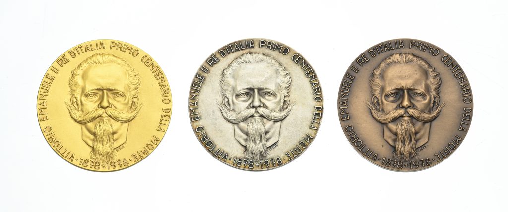 Tre medaglie commemorative di Savoia - oro, argento e bronzo - presentano ciascuna il ritratto in rilievo di un uomo barbuto con i baffi arricciati e un testo in italiano intorno al bordo. Le medaglie celebrano il primo centenario dell'Italia, 1878-1978.