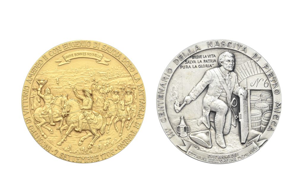 Due medaglie commemorative di Savoia: una in oro, raffigurante una scena di battaglia di cavalleria; l'altra in argento, raffigurante un uomo con botti e torcia in mezzo a un testo in italiano, in onore di Pietro Micca.