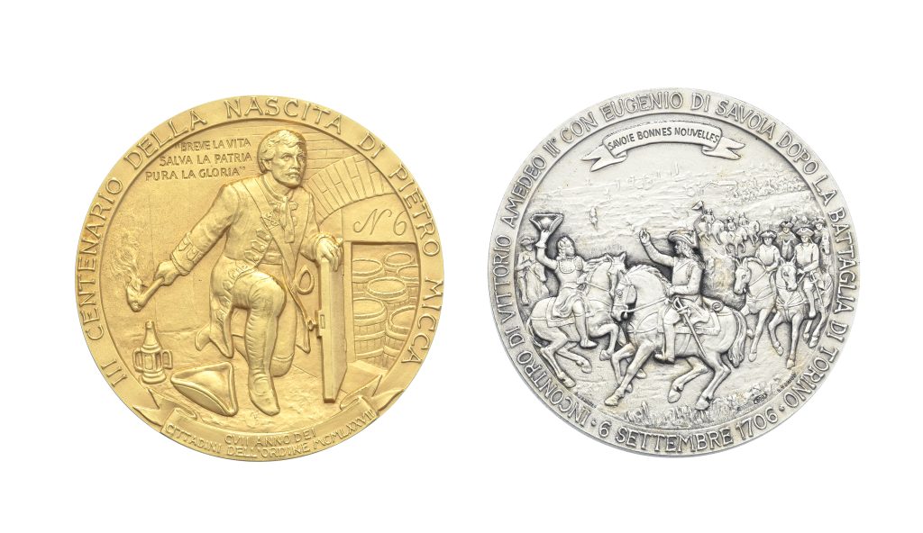 Due medaglie commemorative di Savoia: una dorata raffigurante Pietro Micca con torcia e barile e una argentata con scena di battaglia di cavalleria, entrambe con iscrizioni in italiano sui bordi.