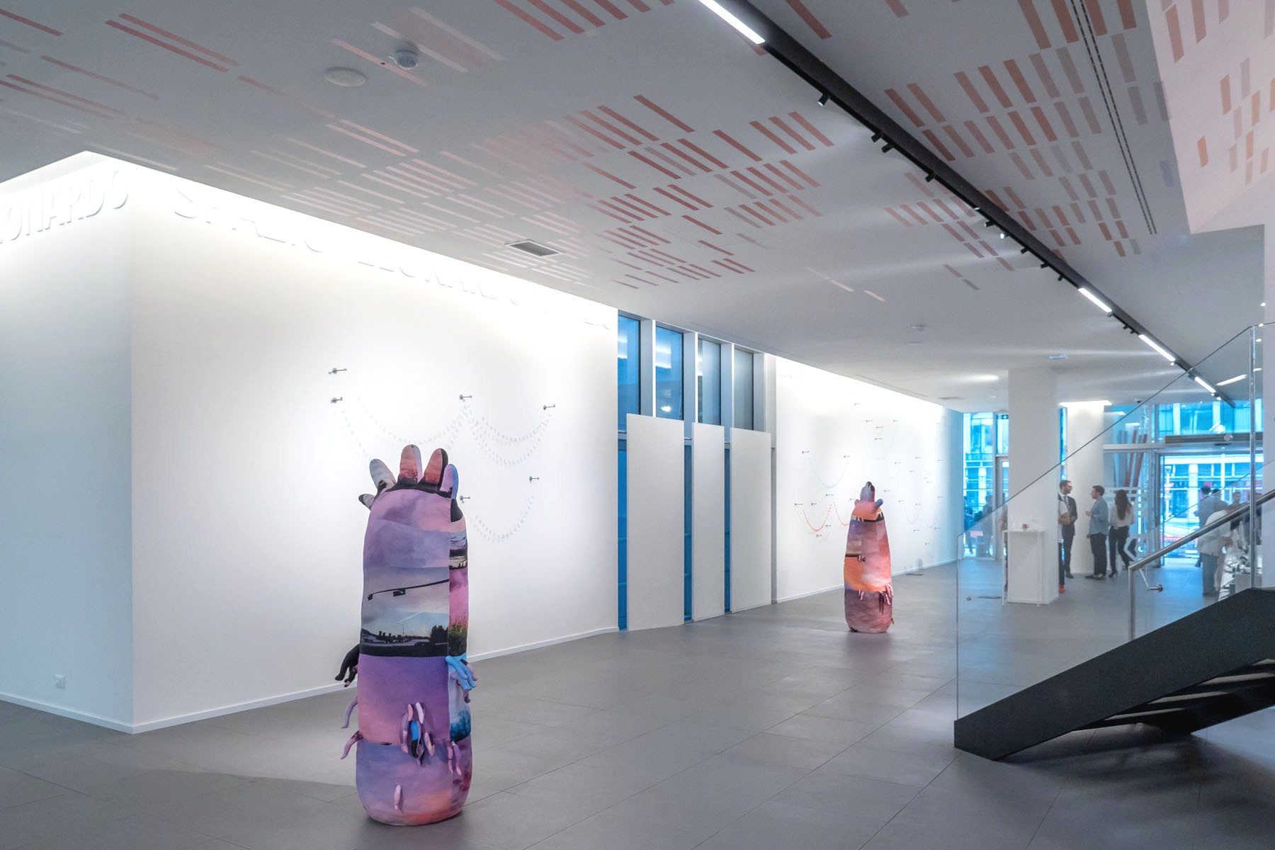 Una galleria d'arte moderna con pareti bianche e luminose, pavimenti in piastrelle grigie e sculture astratte color pastello; l'arte minimalista alle pareti aggiunge eleganza, mentre alcuni visitatori si fermano vicino all'ingresso in vetro: un'atmosfera ispirata a Leonardo Assicurazioni arte.