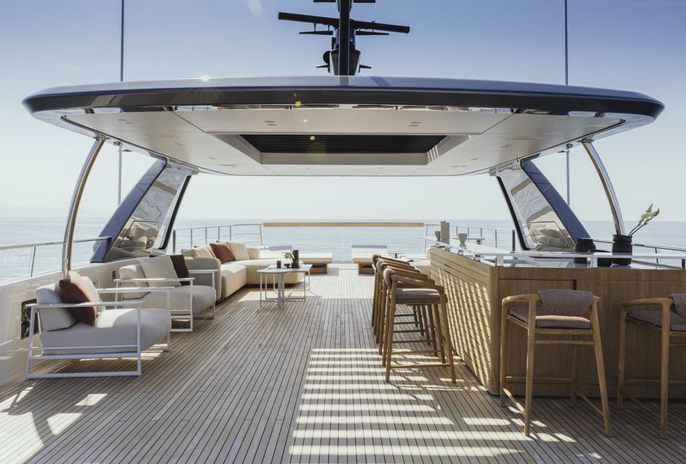 Lussuoso ponte per yacht con moderni arredi da esterno firmati Nautica Italia, con divani, sedie e un bar in legno con sgabelli, che si affaccia sull'oceano sotto un'area coperta in una giornata di sole.