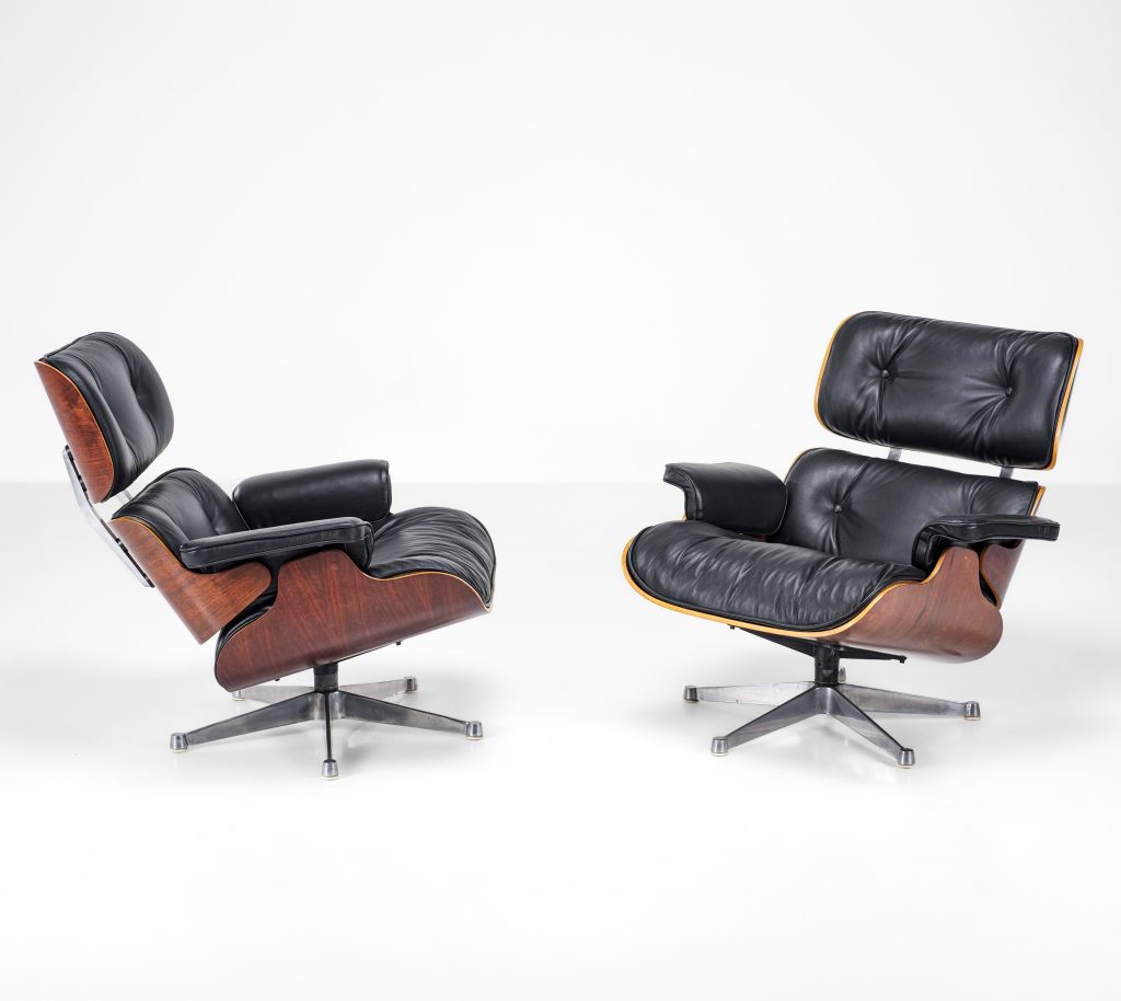 Due poltrone lounge in pelle nera con rivestimento in legno e basi girevoli in metallo, icone del design moderno, sono posizionate su un pavimento bianco su uno sfondo bianco semplice: un look di grande effetto per qualsiasi spazio in questa asta settembre.