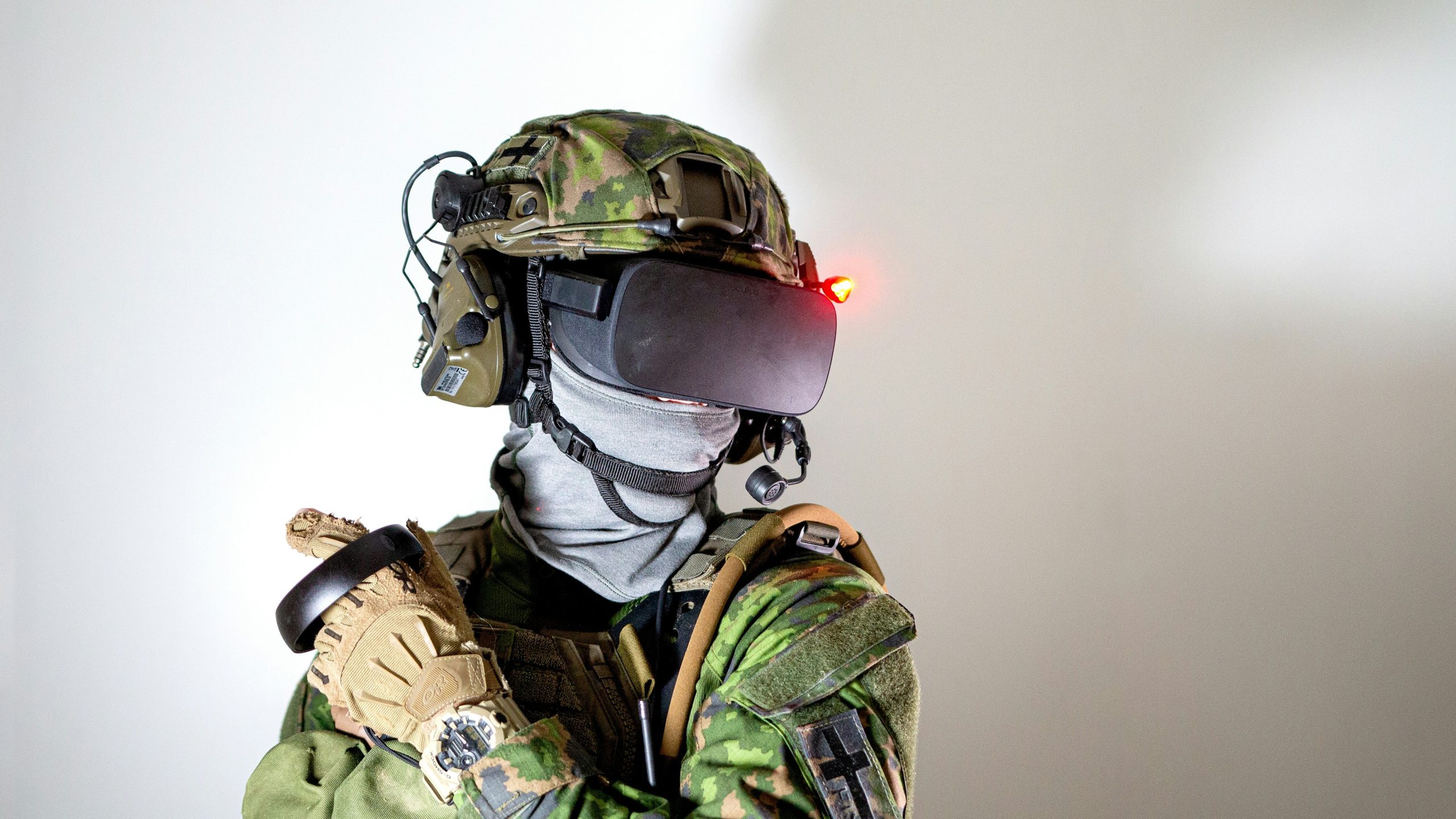 Una persona in tenuta mimetica militare e guanti, che rappresenta investire difesa Europa USA, indossa una cuffia per la realtà virtuale con una luce rossa, cuffie e microfono, su uno sfondo bianco.