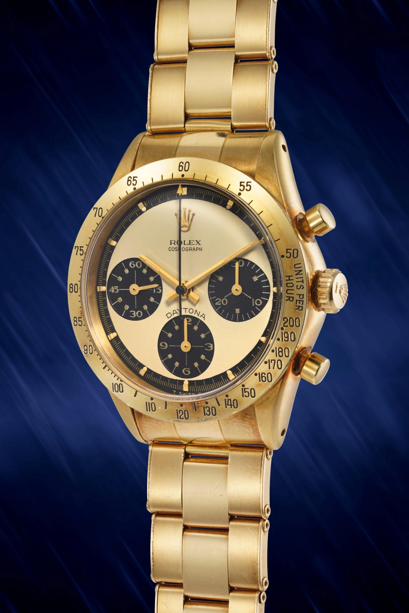 Un orologio da polso Rolex Daytona in oro con quadrante nero e oro, tre contatori e un bracciale in oro, esposto su uno sfondo blu scuro strutturato - un pezzo iconico visto all'asta 10 anni Phillips.