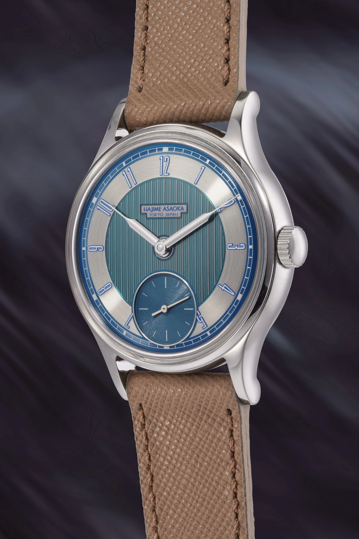 Un orologio da polso di lusso con cinturino in pelle testurizzata marrone chiaro, cassa argentata, quadrante blu e argento e quadrante dei piccoli secondi: un'eleganza che si vede spesso in un'asta 10 anni Phillips, su uno sfondo viola scuro e sfocato.