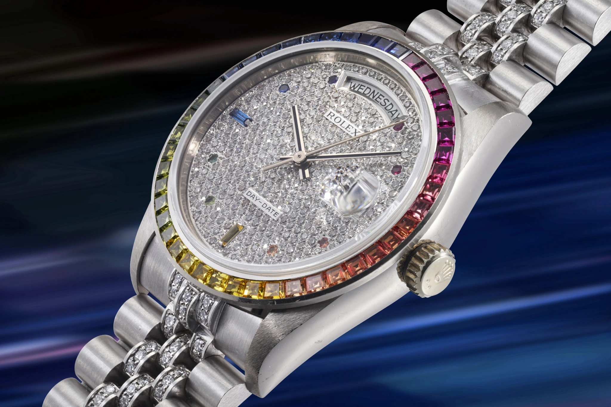 Un lussuoso orologio Rolex con quadrante tempestato di diamanti, gemme color arcobaleno intorno alla lunetta e bracciale in metallo argentato brilla elegantemente - ricordando i pezzi rari visti a un'asta 10 anni Phillips - su uno sfondo blu e viola sfocato.