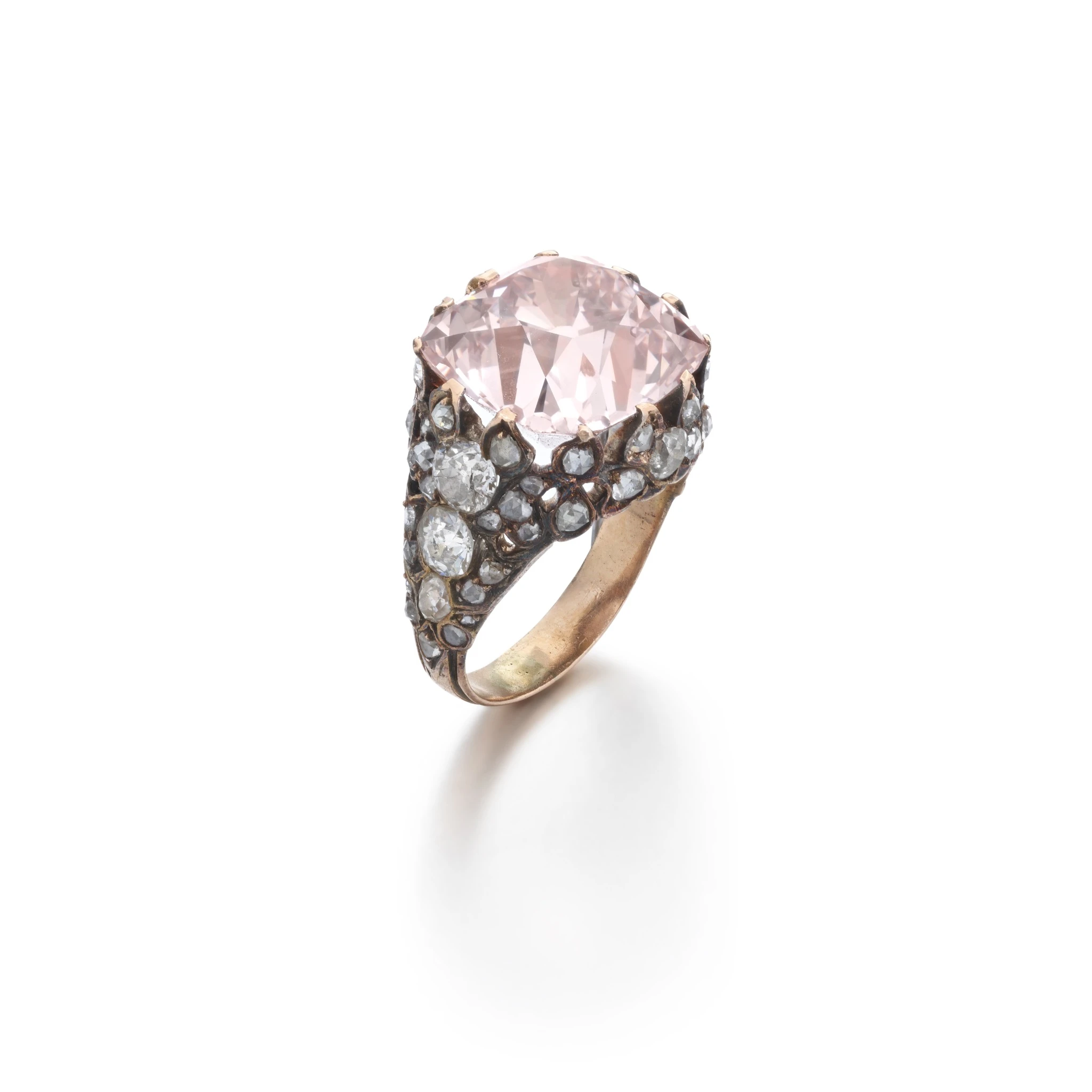 Anello in oro con una grande gemma ovale di colore rosa pallido al centro, circondata da diamanti rotondi più piccoli incastonati in una fascia ornata in stile vintage.