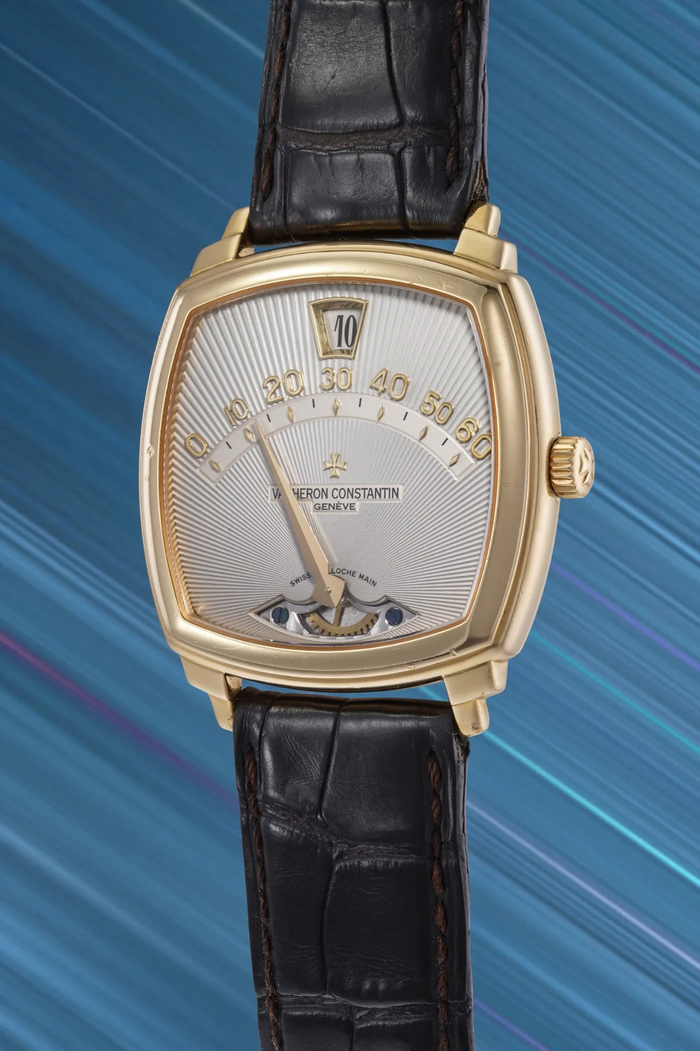 Orologio Vacheron Constantin in oro di una collezione prototipo, con cinturino in pelle, quadrante argentato, indicazione retrograda e finestrella delle ore saltanti, su uno sfondo dinamico a striature blu e viola.