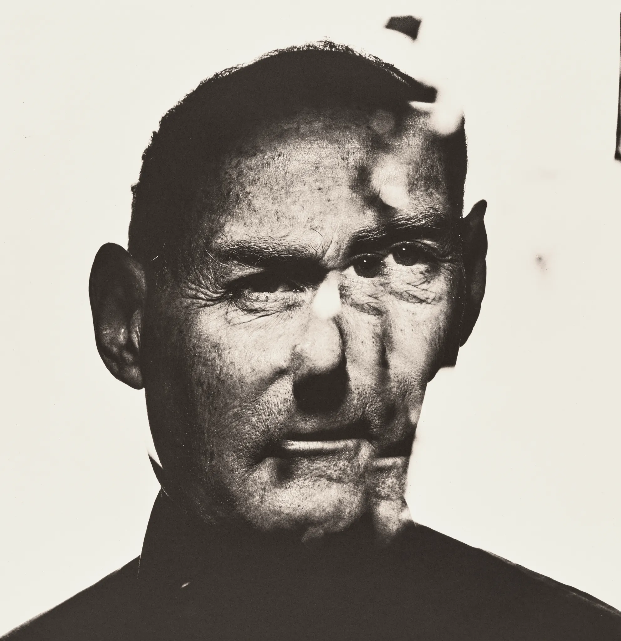 Il ritratto in bianco e nero del volto di un uomo anziano è distorto da un effetto di sfocatura e doppia esposizione, che richiama lo stile astratto e surreale visto nelle fotografie di Irving Penn asta su uno sfondo semplice.