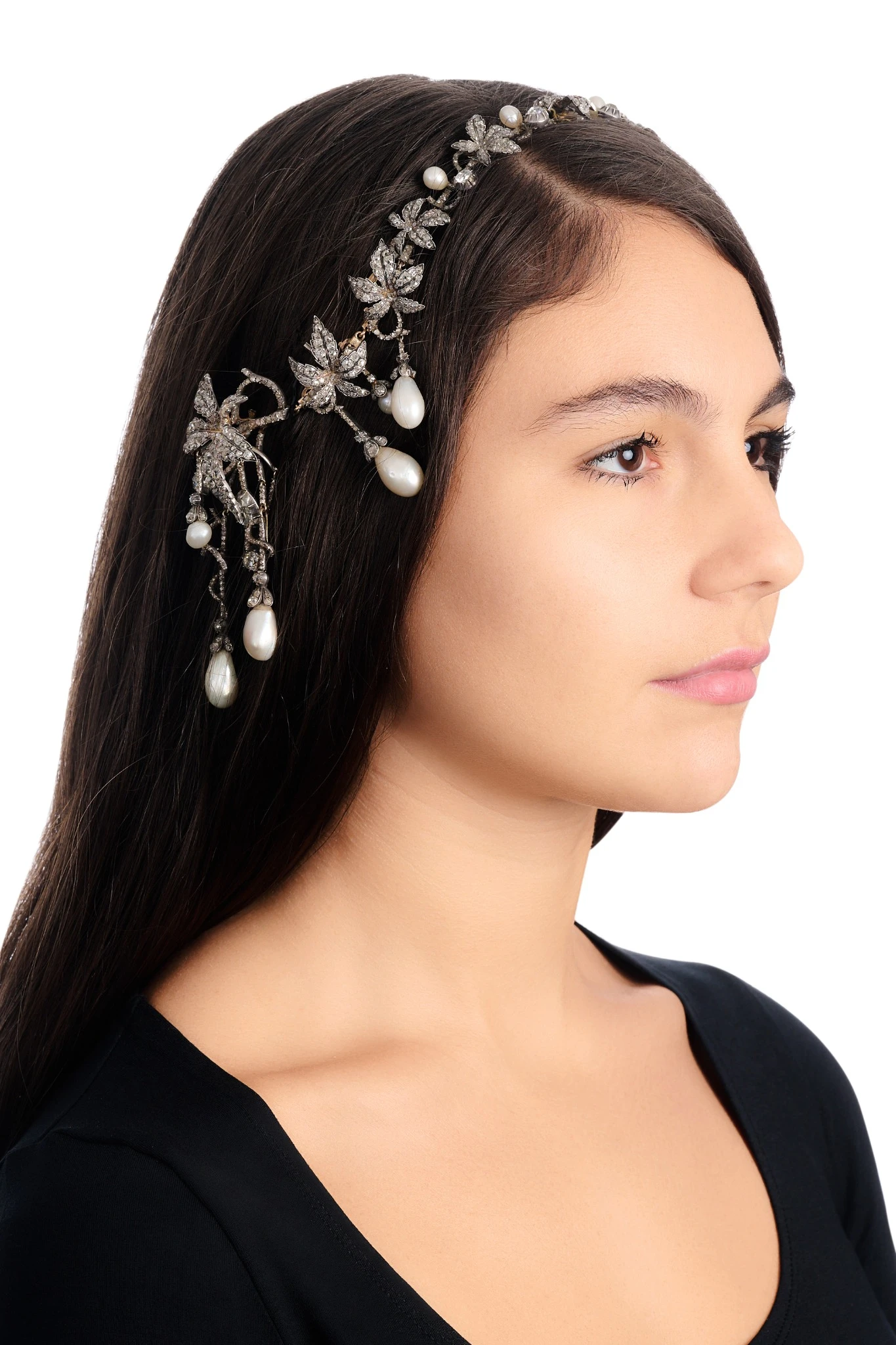 Una donna dai lunghi capelli scuri indossa un copricapo decorato con foglie d'argento, pietre scintillanti che ricordano i diamanti napoleonici e perle pendenti, su uno sfondo bianco.
