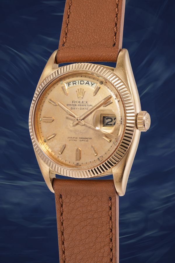 Orologio Rolex Oyster Perpetual Day-Date d'oro con cinturino in pelle marrone, con indicazione del venerdì e della data su uno sfondo blu a spirale.