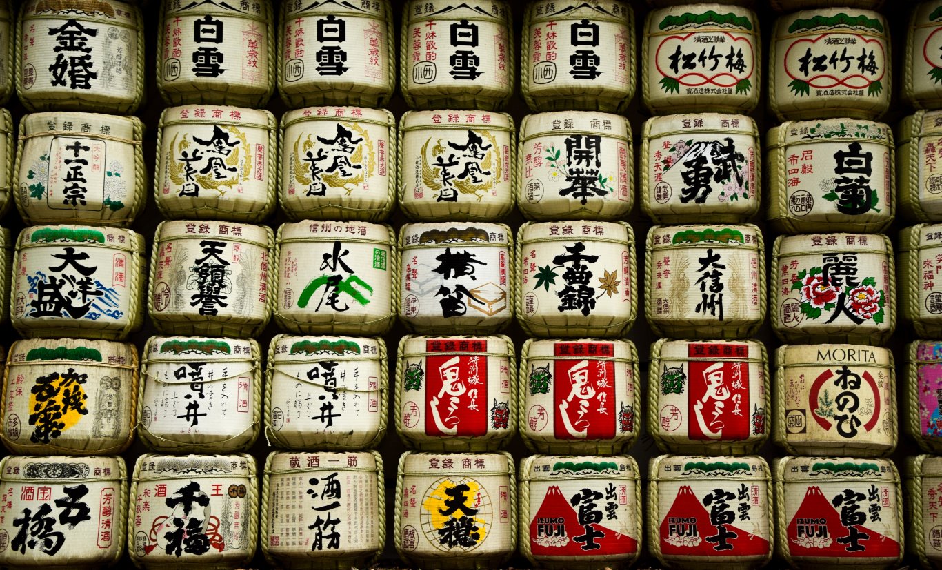 Pile di botti di sakè tradizionali giapponesi decorate con caratteri e simboli kanji colorati, disposte in file e utilizzate per scopi cerimoniali.