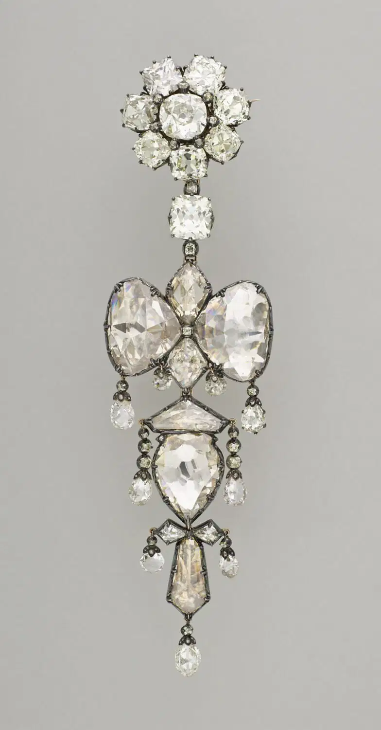 Un'ornata spilla di diamanti del XVIII secolo, che ricorda i tesori coinvolti nel furto gioielli del Louvre, presenta grandi diamanti taglio rosa in un disegno simmetrico, floreale e a nastro, incastonati in argento con eleganti gocce di diamante.