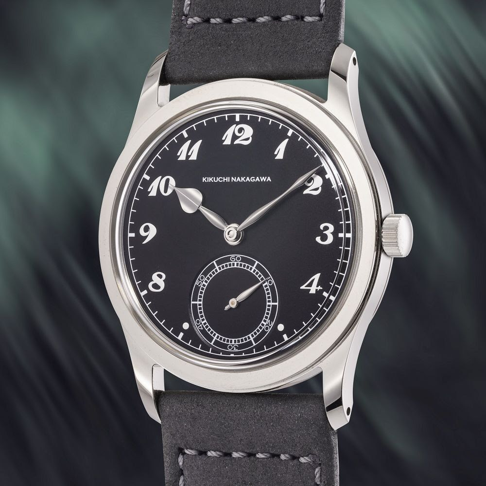Orologio da polso di lusso con quadrante nero, cassa argentata, cifre bianche e quadrante dei piccoli secondi a ore 6. Kikuchi Nakagawa, rinomato per gli orologi giapponesi di lusso, è stampato sotto le 12, abbinato a un cinturino in pelle nera.