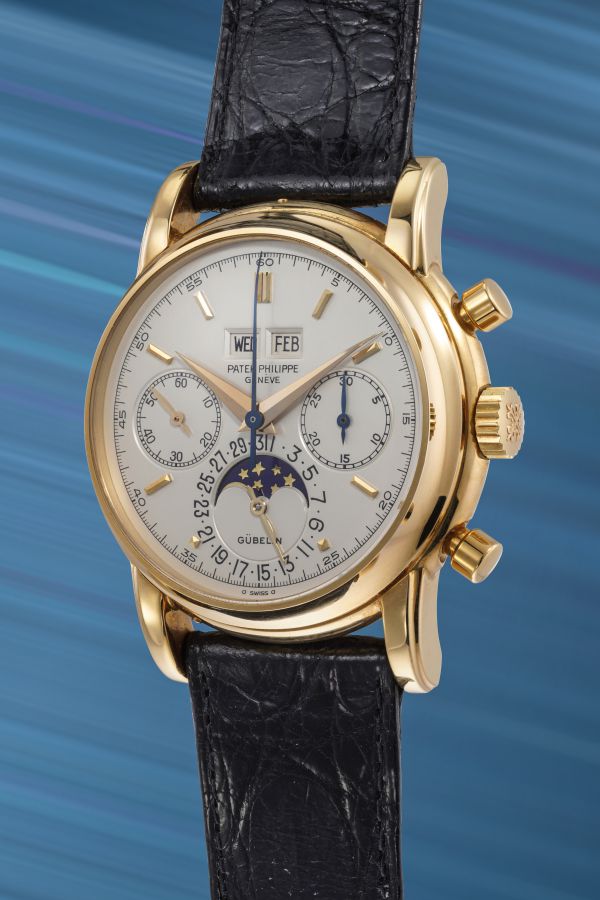 Un orologio da polso Patek Philippe in oro con quadrante bianco, cinturino in pelle nera, tre contatori, indicazione delle fasi lunari e finestrelle del giorno e del mese - uno squisito esemplare ispirato al patek philippe più costoso - mostrato su uno sfondo blu sfocato.