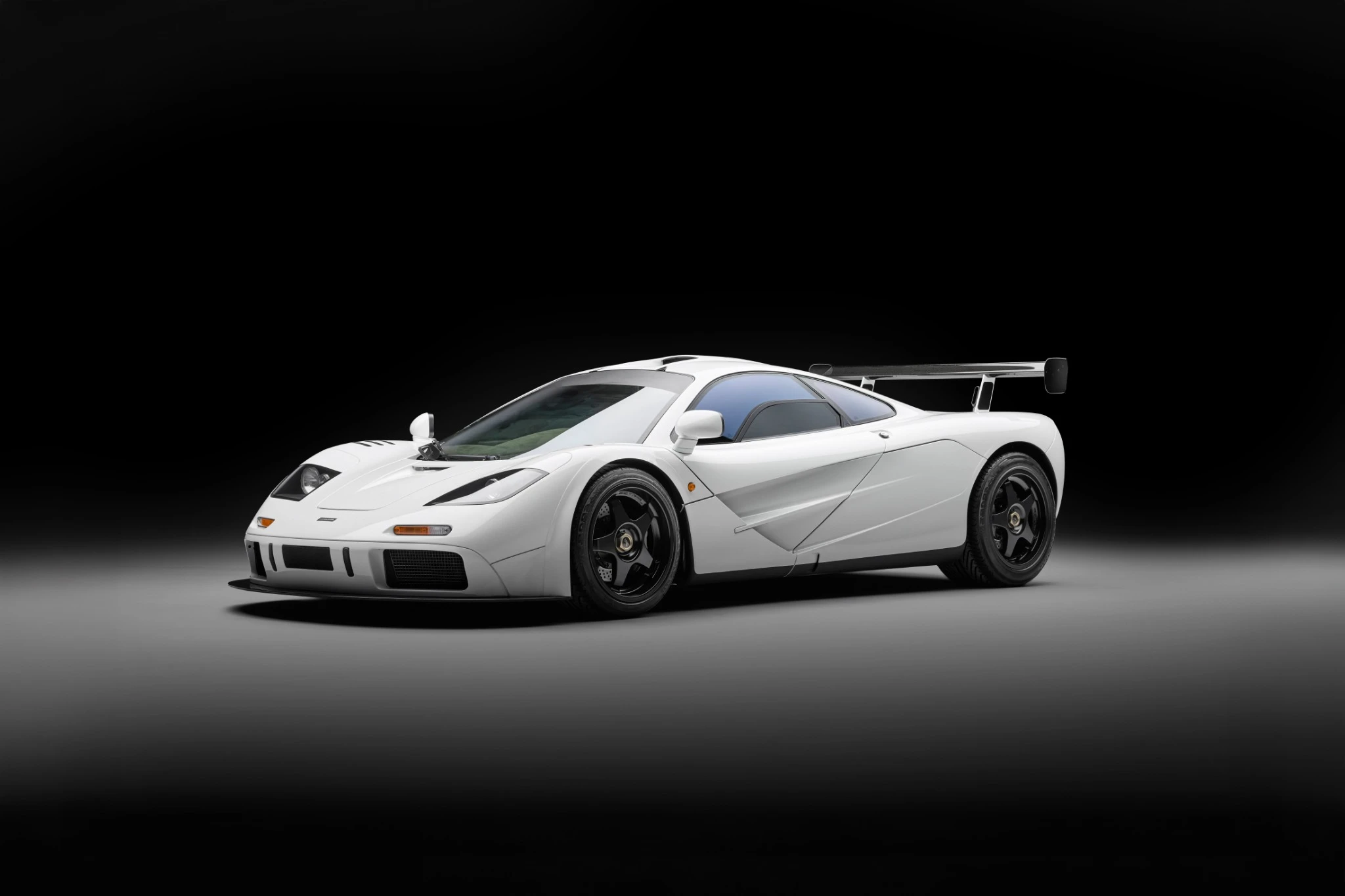Un'auto sportiva McLaren F1 bianca è esposta in uno studio con sfondo nero, caratterizzata da curve aerodinamiche, ruote nere e un grande spoiler posteriore, vera icona dello stile lusso di Abu Dhabi.
