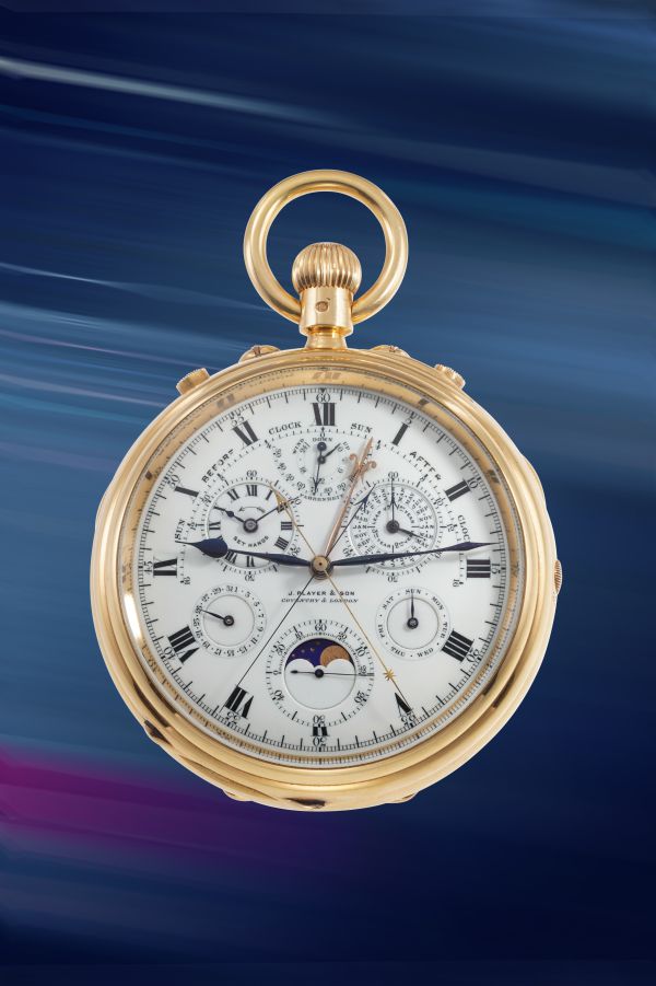 Un orologio da tasca in oro con un quadrante bianco dettagliato che mostra quadranti multipli, numeri romani e indicatori delle fasi lunari - un elegante esempio di orologi costosi 2025 - su uno sfondo blu e viola sfocato.