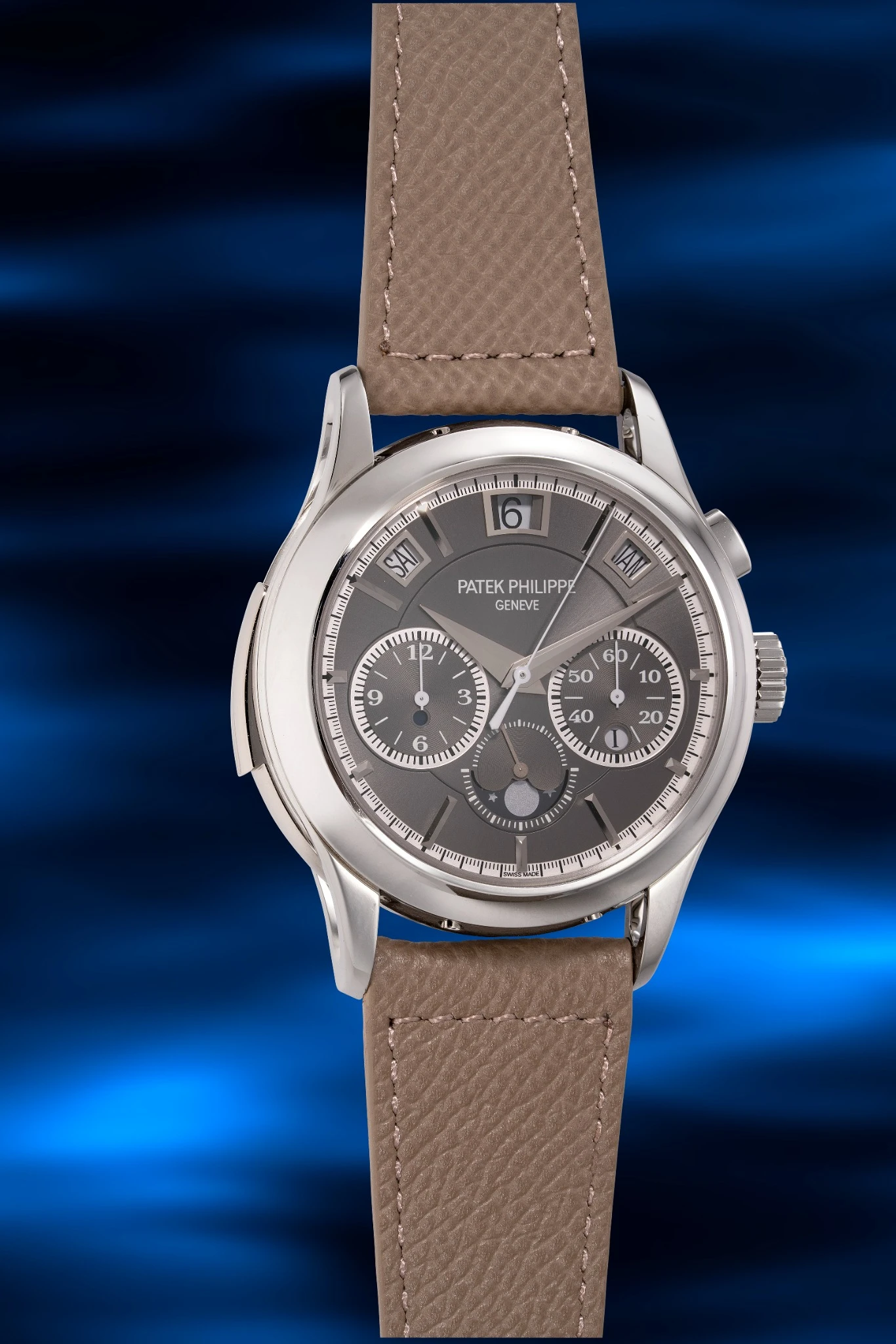 Orologio da polso di lusso Patek Philippe Hong Kong con cinturino in pelle marrone, cassa argentata e quadrante cronografico grigio, visualizzato su uno sfondo blu leggermente sfocato.