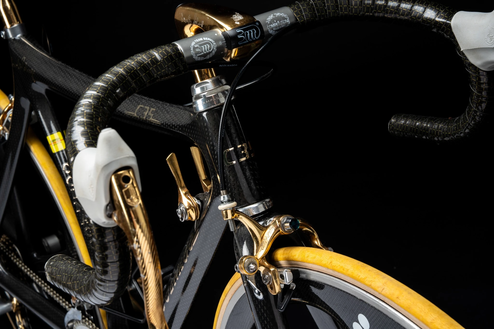 Primo piano della parte anteriore di una bicicletta che mostra il manubrio, la leva del freno e parte del telaio. La bicicletta è caratterizzata da dettagli neri e oro con pneumatici gialli, che creano un'atmosfera da Abu Dhabi Lusso su uno sfondo nero.