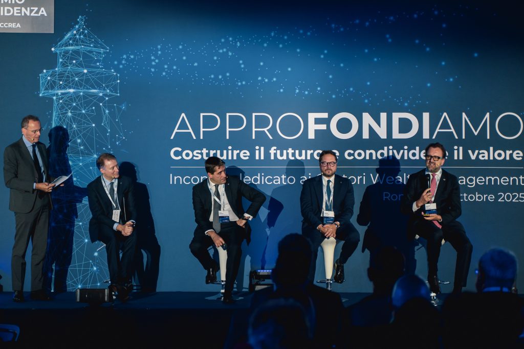 Cinque uomini in giacca e cravatta partecipano a una tavola rotonda su uno sfondo blu con testo italiano bianco e una grafica digitale del faro; un uomo parla al microfono mentre gli altri ascoltano.