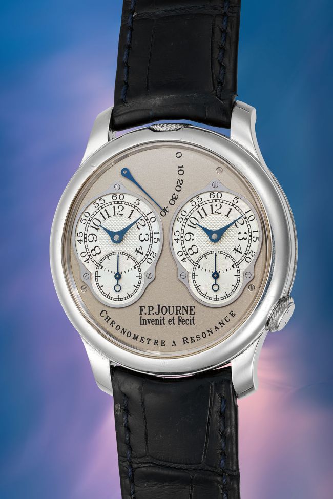 Lussuoso orologio da polso F.P. Journe Chronomètre à Résonance con due quadranti, lancette blu e cinturino in pelle nera, su sfondo blu e rosa sfumato.