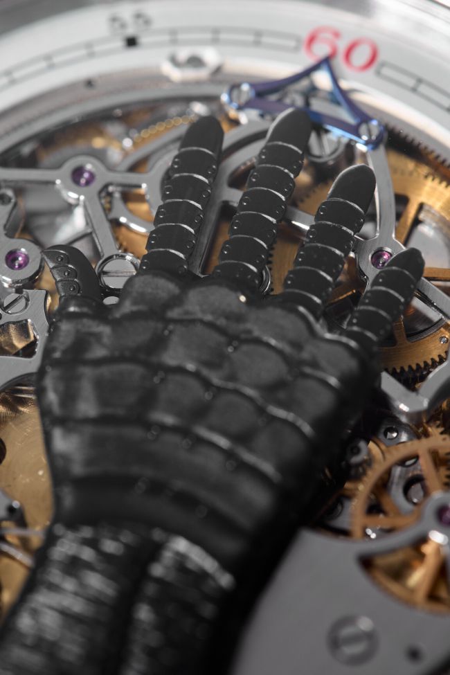 Primo piano del quadrante di un orologio di lusso con ingranaggi e meccanismi intricati, con una lancetta meccanica o robotica nera appoggiata sopra i componenti.
