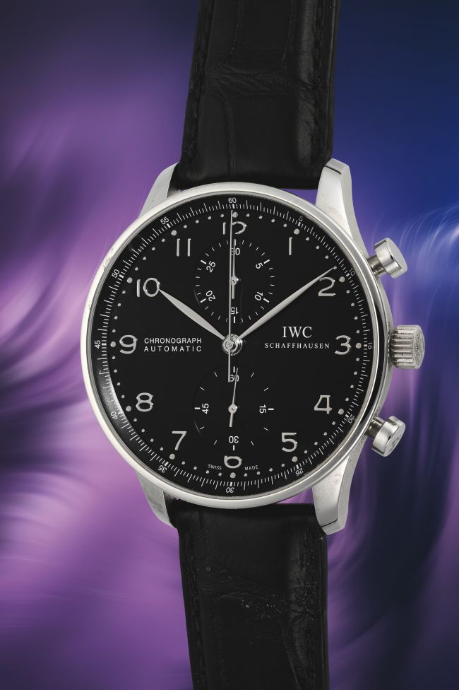 Un orologio da polso cronografo IWC Schaffhausen con quadrante nero e cinturino in pelle nera, che richiama il classico stile dell'orologio Coppola, visualizzato su un vivace sfondo viola e blu.