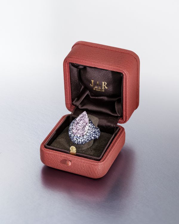 Anello con una grande gemma rosa a forma di pera circondata da numerose pietre blu mellon diamantate rotonde incastonate a grappolo.