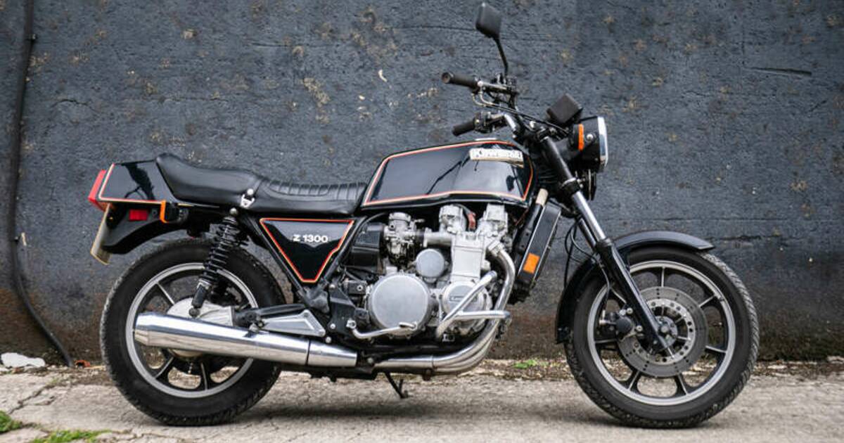 Una classica moto Kawasaki Z1300 nera con dettagli cromati è parcheggiata su una superficie di cemento di fronte a un muro grigio scuro, che ricorda le moto iconiche di Harry Metcalfe.