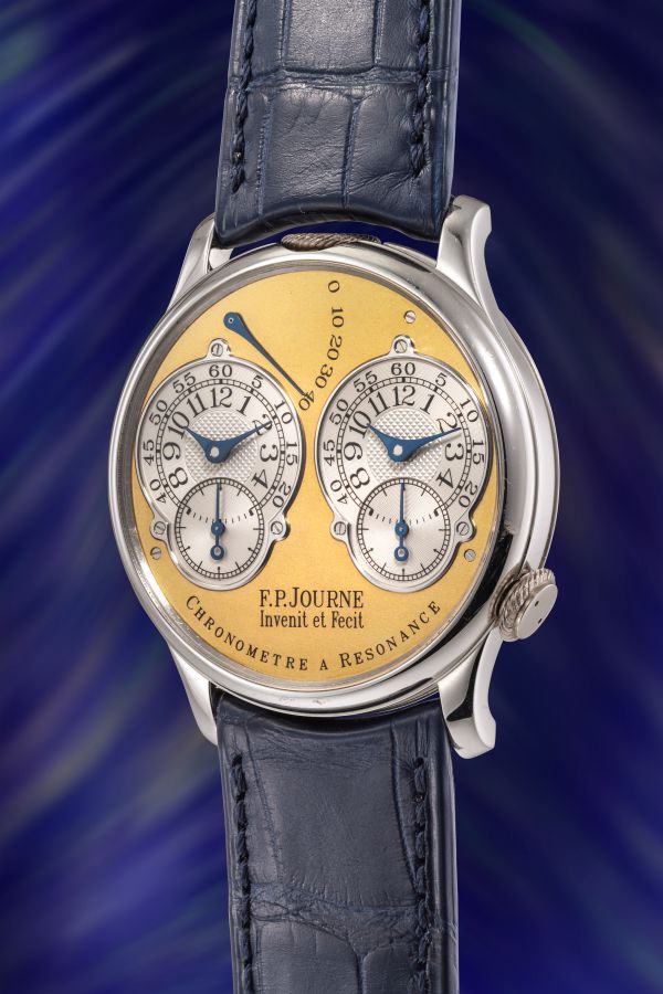 Un lussuoso orologio da polso F.P. Journe con quadrante in oro, doppi quadranti, lancette blu e cinturino in pelle blu è esposto su uno sfondo vorticoso blu e viola: uno squisito esempio di orologi costosi 2025.