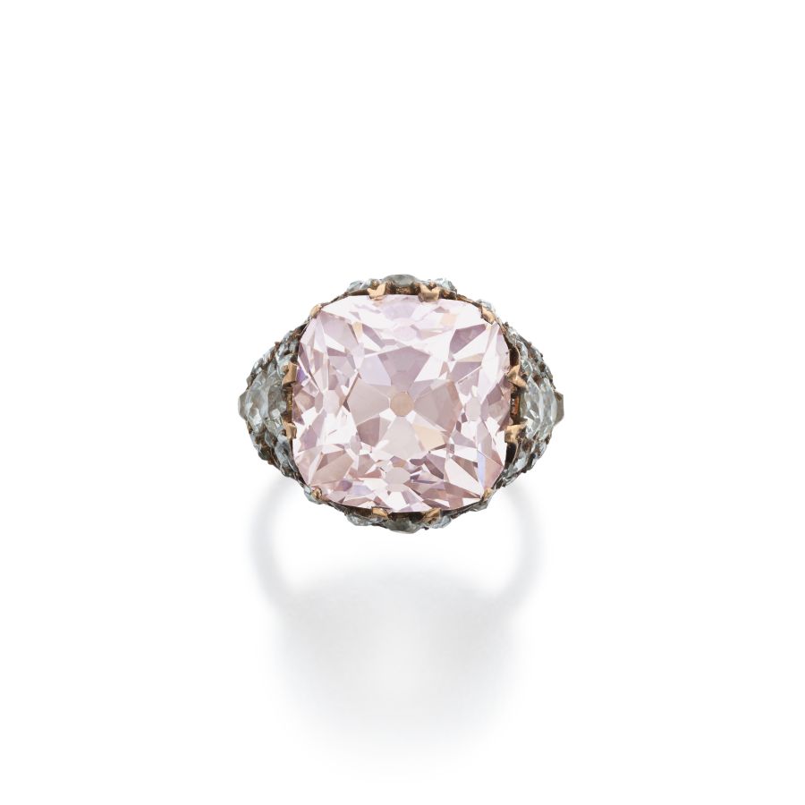 Anello con grande gemma rosa pallido tagliata a cuscino e incastonata in una fascia di metallo ornata, su sfondo bianco.