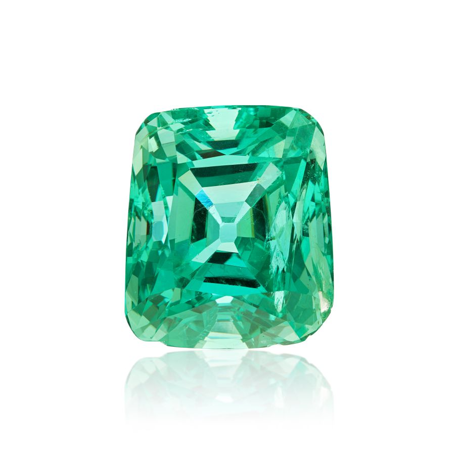 Una vibrante gemma di smeraldo tagliata a cuscino con una ricca tonalità verde, che riflette la luce e mostra intricate sfaccettature, incastonata su uno sfondo bianco.