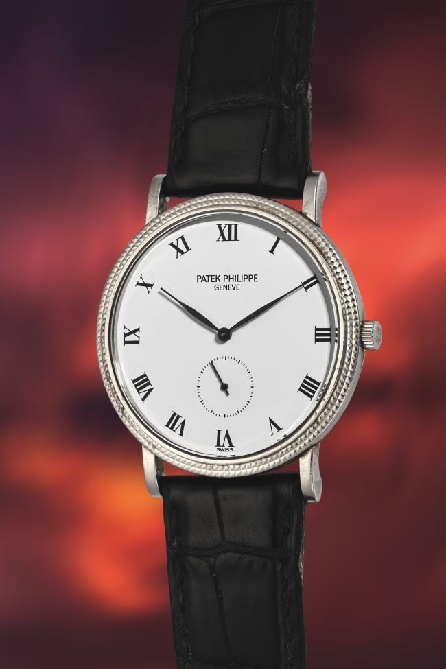 Un classico orologio da polso Patek Philippe, ispirato allo stile dell'orologio Coppola, con quadrante bianco, numeri romani neri, quadrante dei piccoli secondi e cinturino in pelle nera su uno sfondo sfocato dai toni caldi.