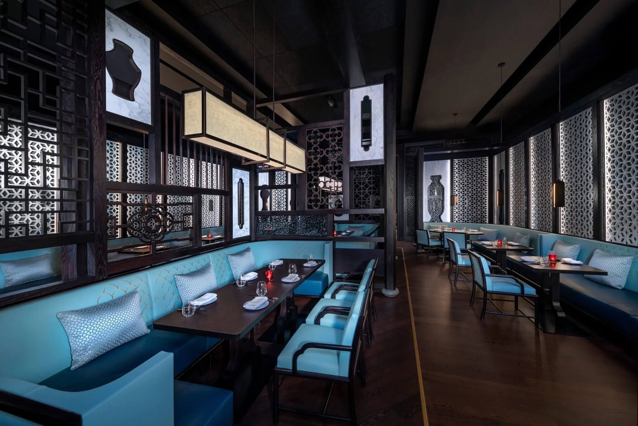 Modern restaurant interior with elegant blue seating, dark wooden tables, and decorative geometric screens. Soft lighting creates a cozy atmosphere, while patterned walls and artistic vases add a touch of sophistication.