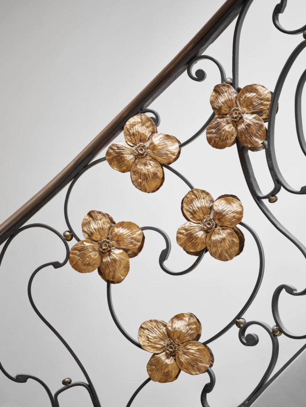 La ringhiera decorativa della scala in metallo presenta ornamenti floreali color oro con quattro petali ciascuno, su uno sfondo bianco e una struttura in ferro scuro e curvilineo, che ricorda l'estrosa arte di Ippopotamo Lalanne.